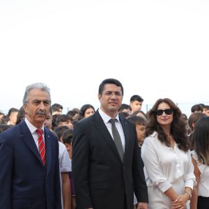 Açık havada öğrencilerin önünde yan yana duran, takım elbiseli iki erkek ile beyaz giyimli iki kadın