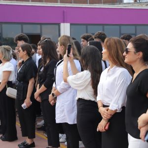 Okul binasının önünde yan yana dizilmiş, siyah ve beyaz giyimli öğretmenler ile yetişkinler