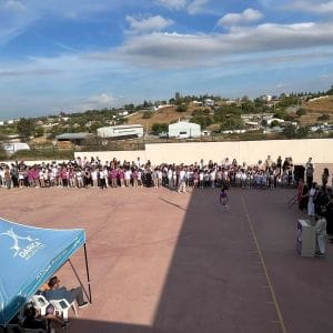 Okul bahçesinde açılış töreni için toplanmış kalabalık öğrenci grubu, solda mavi çadır